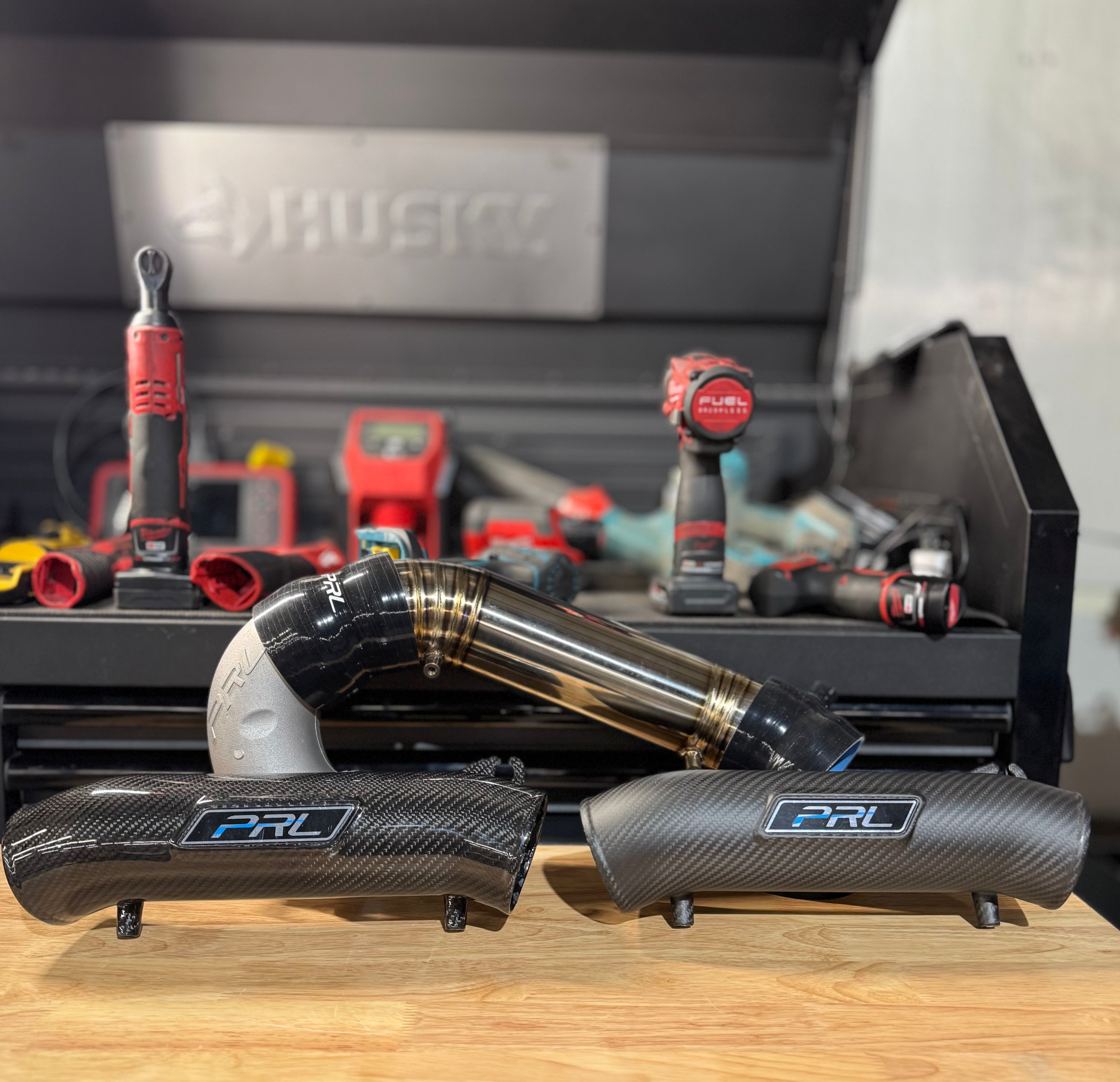 A inlet pipe from PRL Motorsports laid on a workbench, with tools in the background.